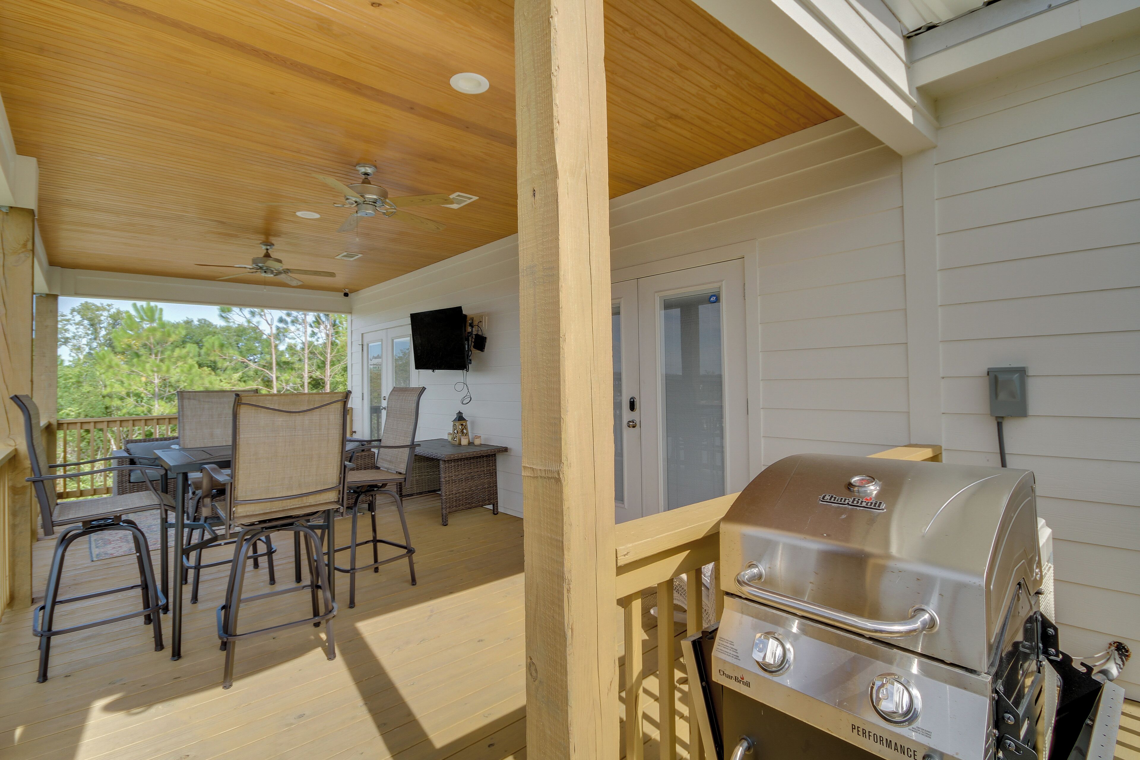 Un'area esterna coperta con un patio in legno, un barbecue e un angolo salotto con sedie e tavolo.