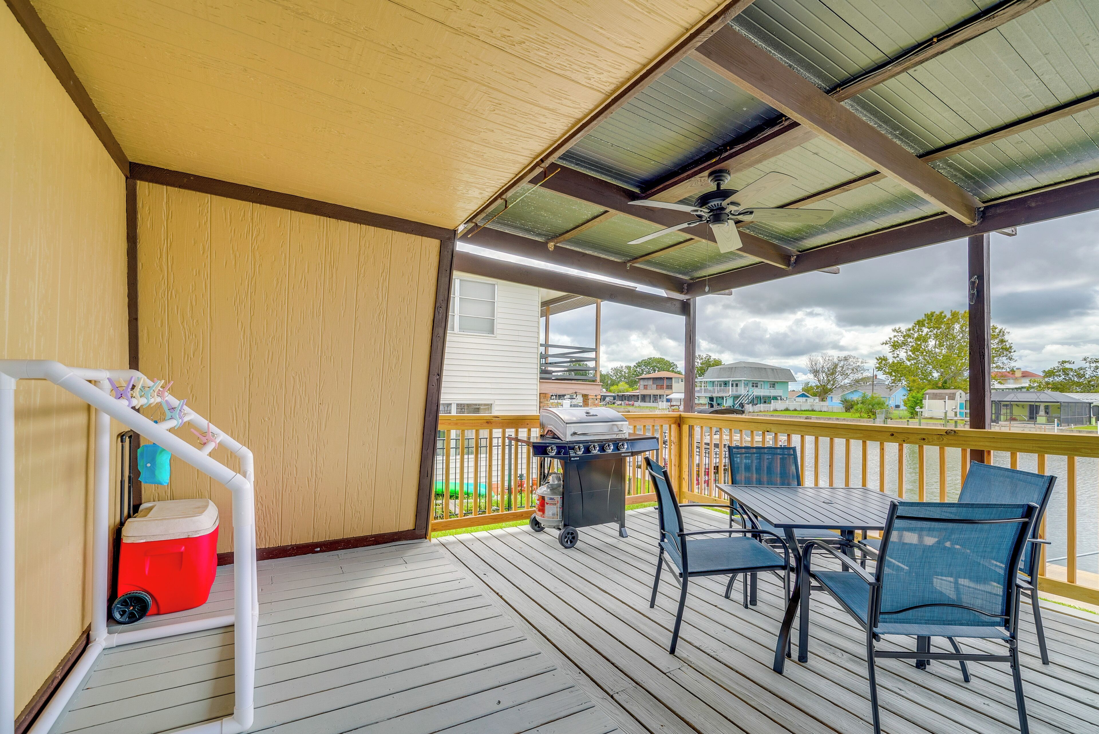 A covered outdoor deck with a grill, chairs, and a cooler.