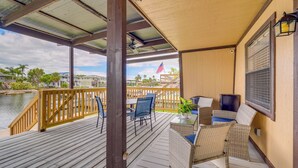 A covered outdoor deck with wooden railings, wicker furniture, and a view of a body of water and buildings in the background.