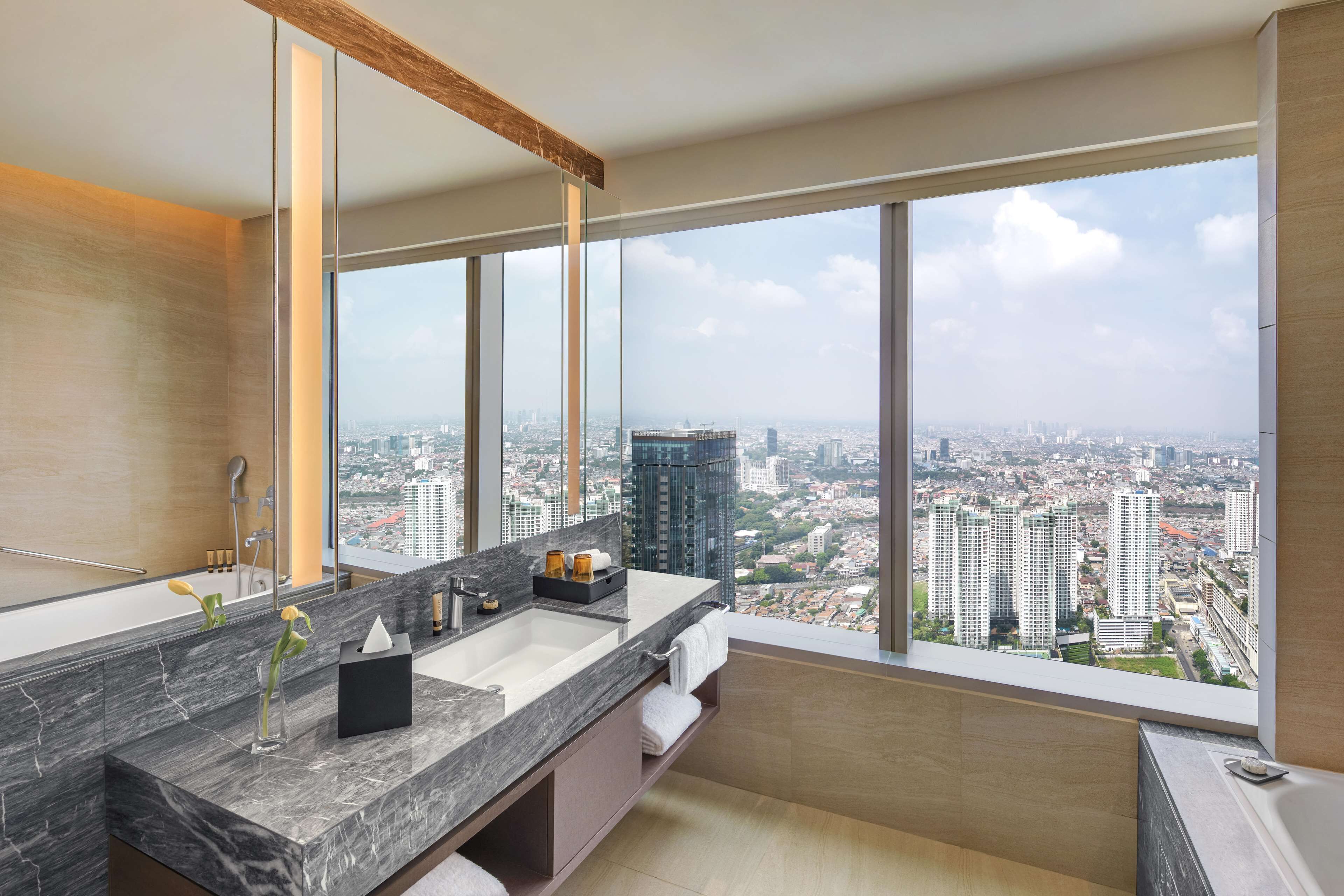 A modern bathroom with a large window, a marble sink, and a city view.
