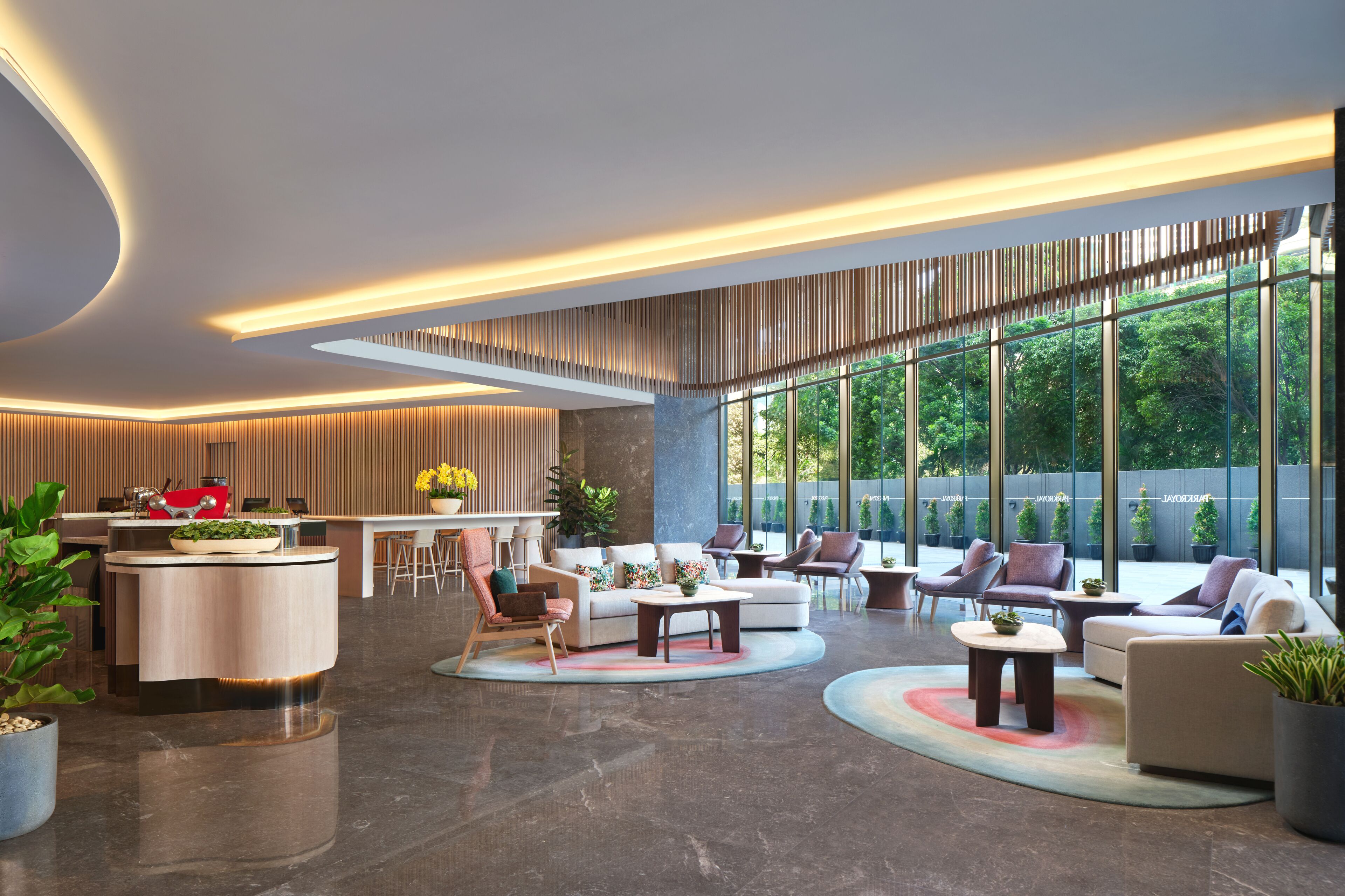 A modern hotel lobby with a central island, seating area, and large windows offering a view of greenery.