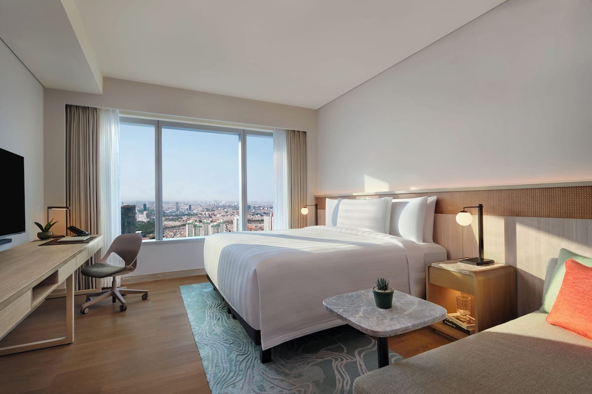 Habitación de hotel con una cama grande, un escritorio, una silla, una mesita, una mesita de noche y una televisión.