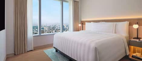 A hotel room with a large bed, a nightstand with a lamp, a view of the city through a large window, and a cityscape visible outside.