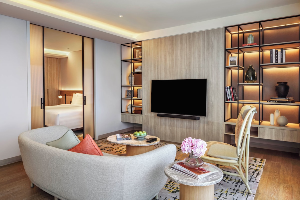 A modern living room with a sofa, a coffee table, a bookshelf, a flat-screen TV, and a chair.