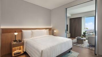 Une chambre d’hôtel moderne avec un grand lit, des lampes de chevet, une table de nuit, une petite table et une vue sur la ville par une grande fenêtre.