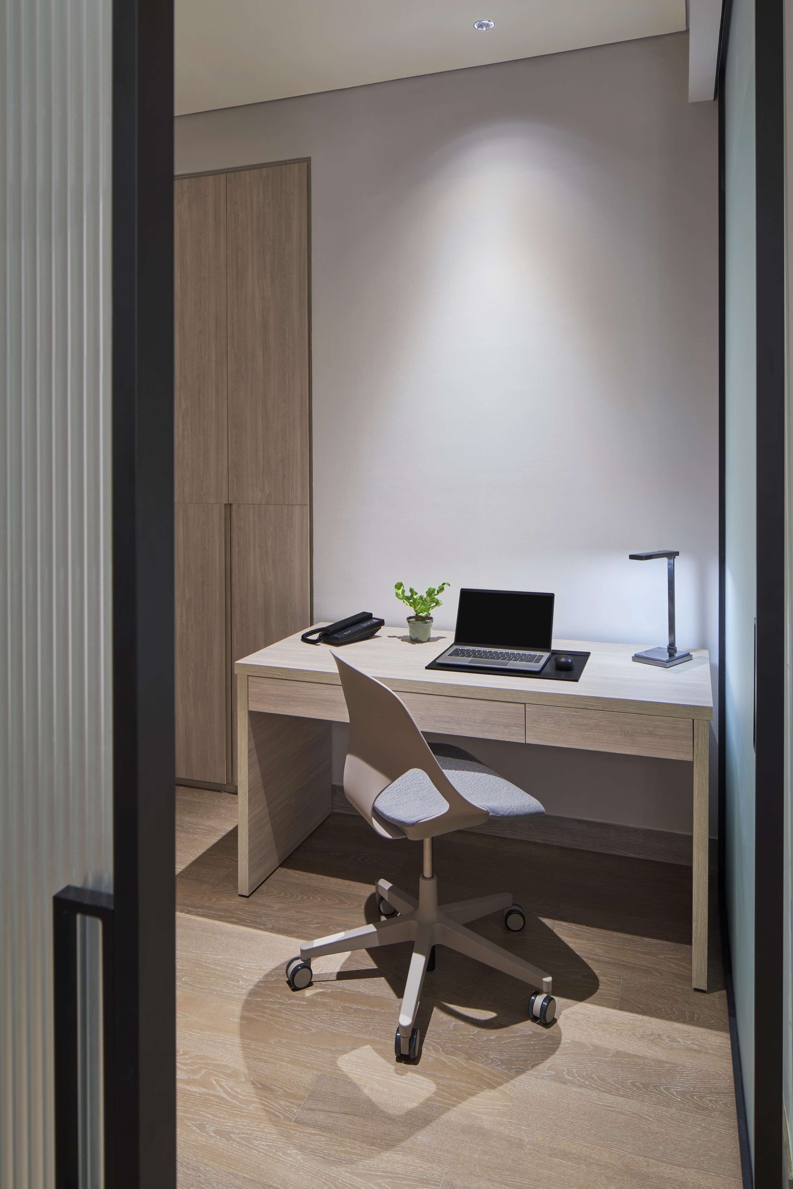 Un espacio de oficina moderno con un escritorio, laptop, silla y una planta pequeña.