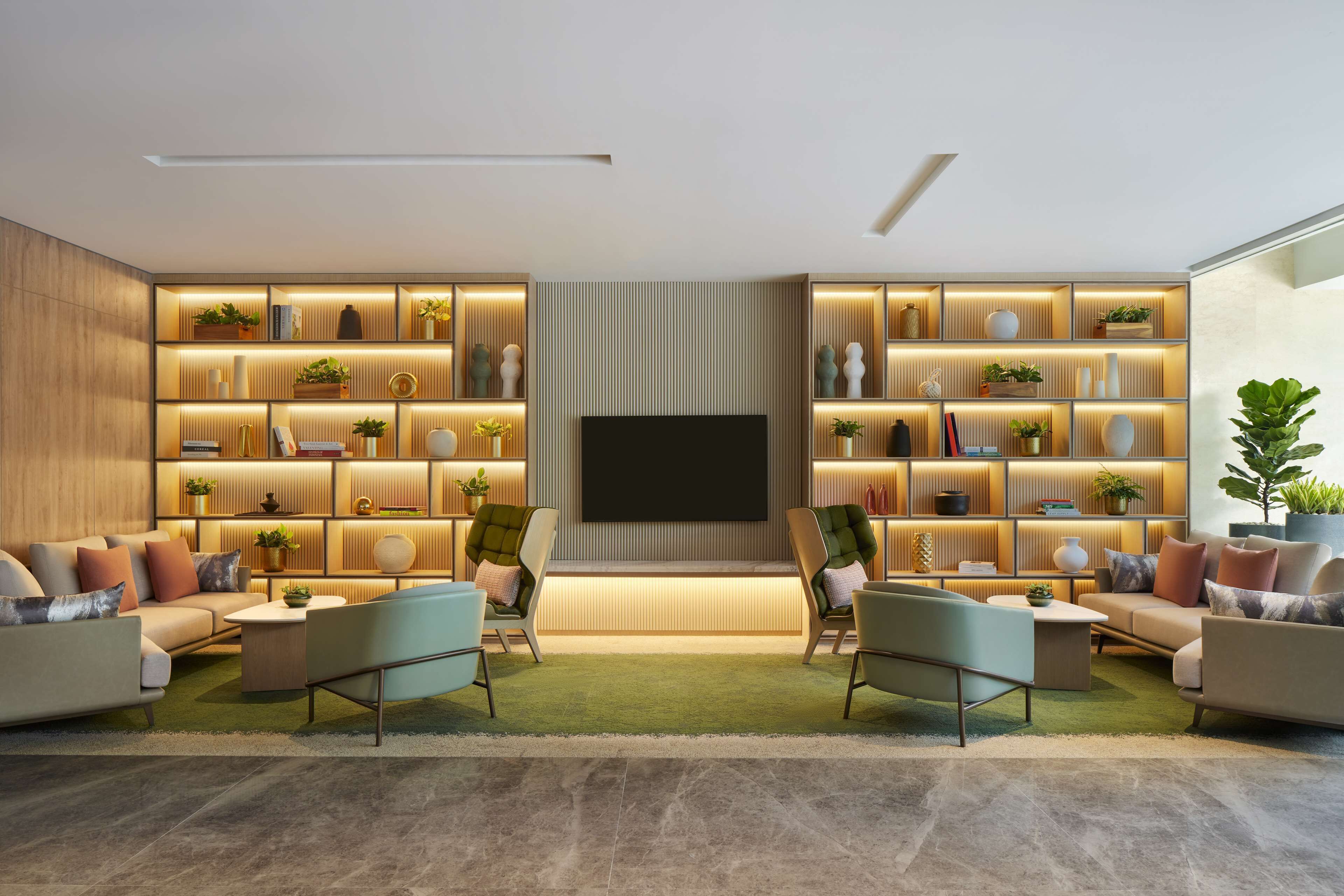 A modern living room with a flat-screen TV, two sofas, a coffee table, and a bookshelf with plants and decorative items.