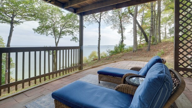 A covered outdoor seating area with wicker furniture and blue cushions, overlooking a body of water and trees. - Waterfront Views: Peaceful Chesapeake Bay Escape (Lusby)