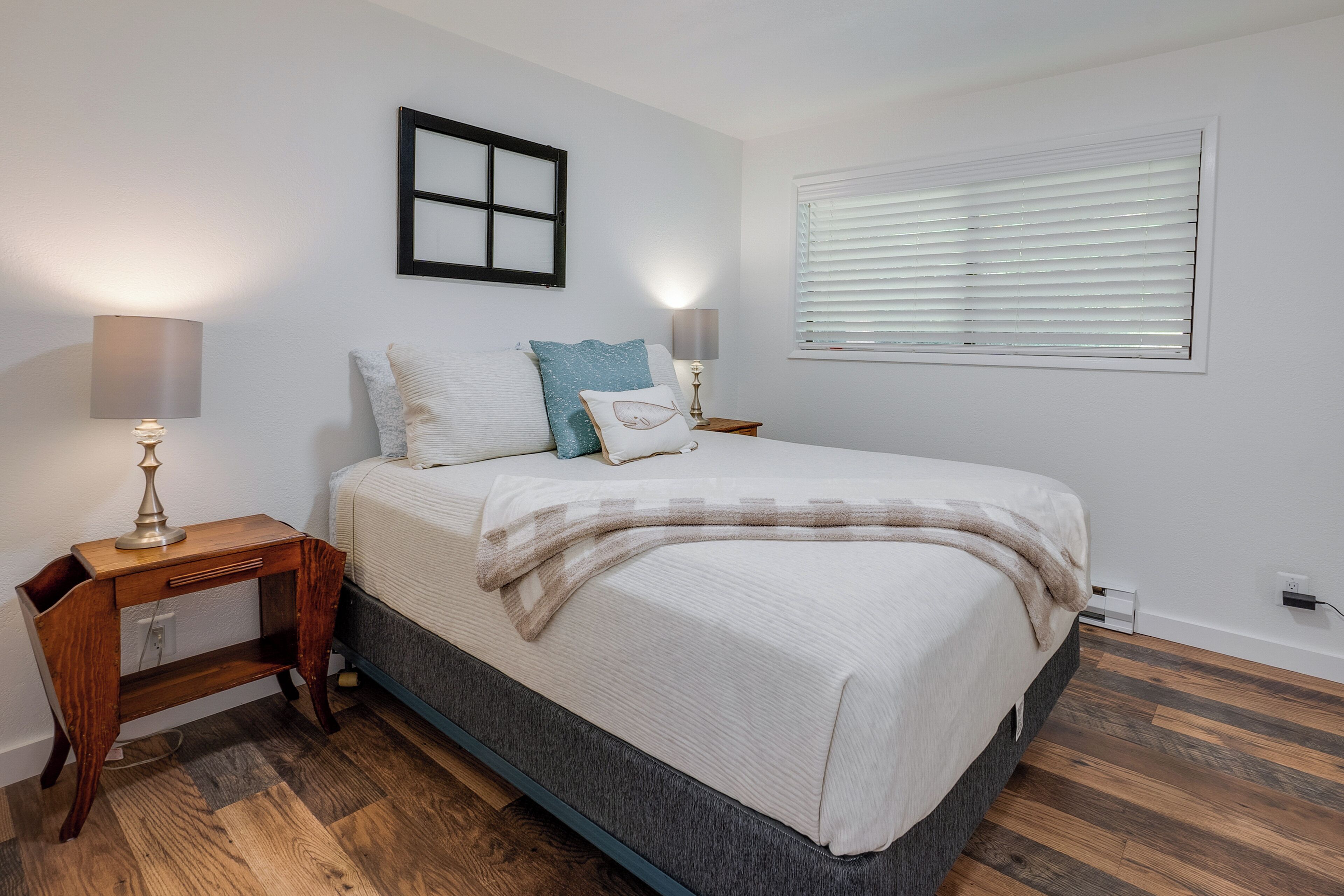 Une chambre à coucher comprenant un lit, des tables de chevet, une lampe, une fenêtre avec des stores et un cadre photo fixé au mur.