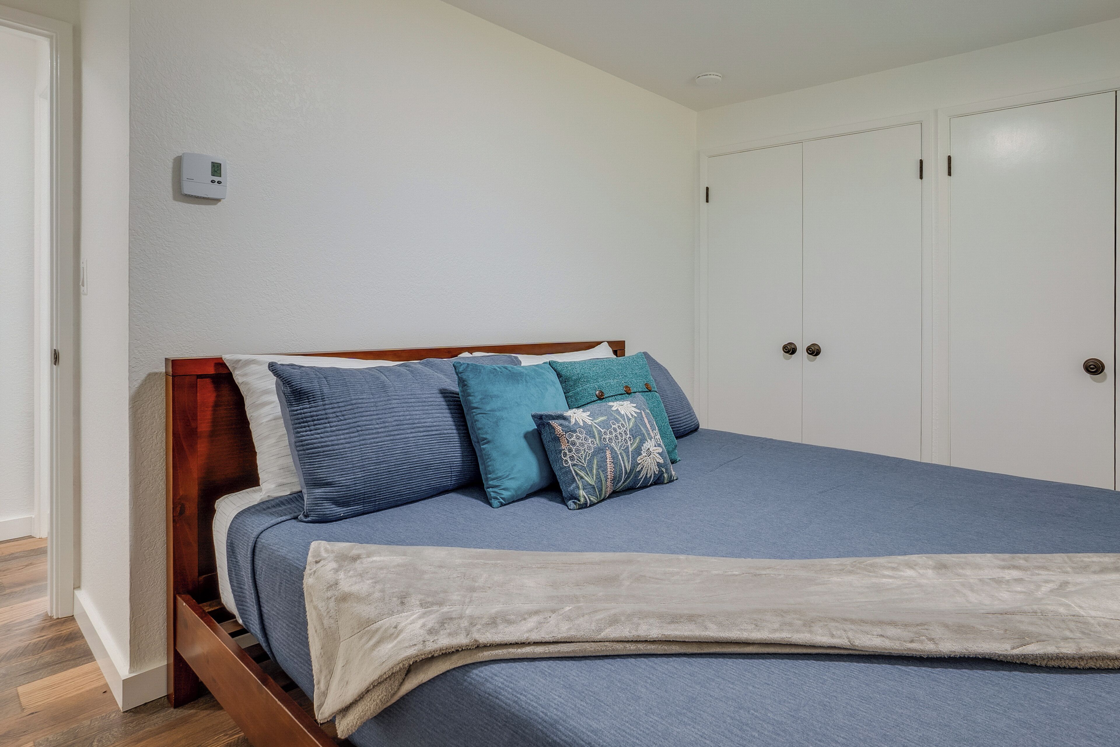 Un dormitorio con estructura de cama de madera, colchón azul y termostato blanco instalado en la pared.