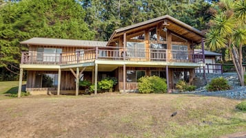 A two-story wooden cabin with a balcony, surrounded by trees and a grassy yard.
