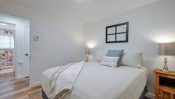 A bedroom with a bed, bedside lamps, a nightstand, a window with blinds, and a door.