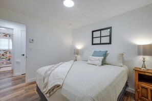 A bedroom with a bed, bedside lamps, a nightstand, a window with blinds, and a door. - Tree-lined Gold Beach Retreat w/ Multiple Decks! (Gold Beach)