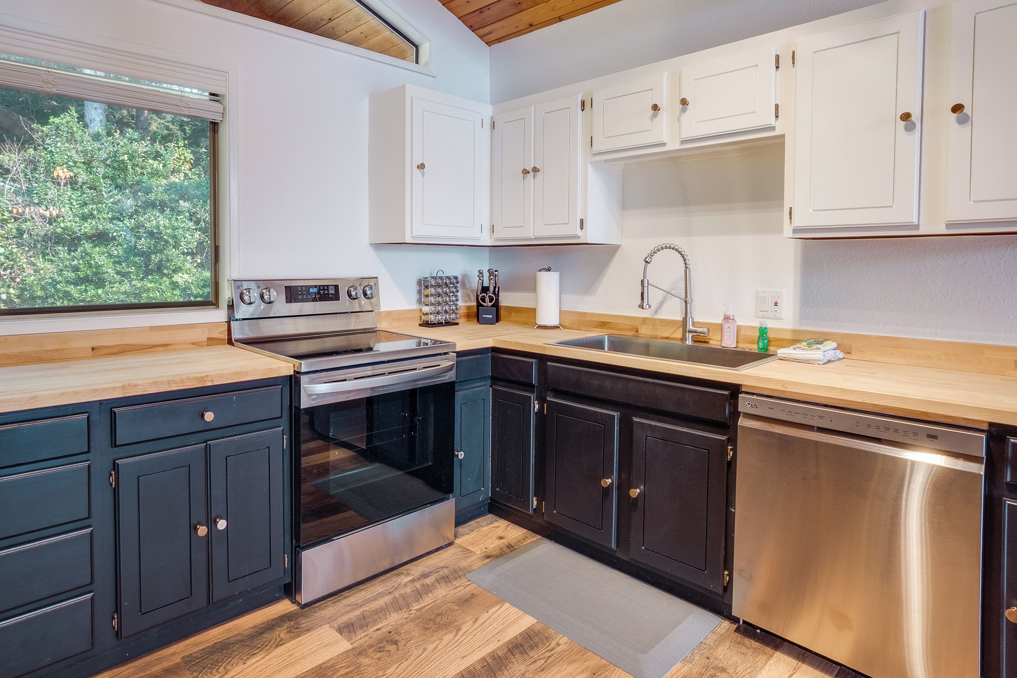 A modern kitchen with black and white cabinetry, stainless steel appliances, and a wooden countertop.