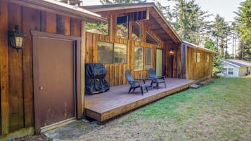 A wooden cabin with a deck, two chairs, and a covered grill area.