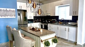 A modern kitchen with white cabinets, a granite countertop, stainless steel appliances, and pendant lighting. - Welcome to Nano’s Home  (La romana)