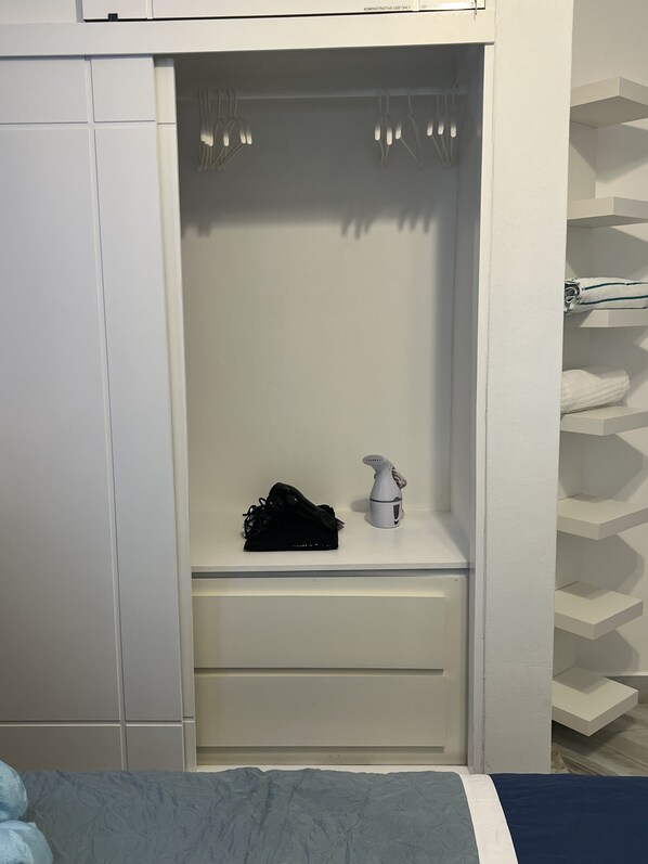 Un dormitorio con un armario blanco, una mesita de noche con secador de pelo y una cama con colcha azul y blanca.