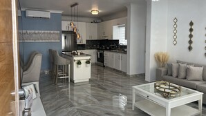 A modern kitchen with white cabinets, a stainless steel refrigerator, and a central island with bar stools. - Welcome to Nano’s Home  (La romana)