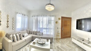 A modern living room with a beige sectional sofa, a glass coffee table, and a flat-screen TV mounted on the wall. - Welcome to Nano’s Home  (La romana)