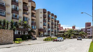 Um edifício residencial com várias andares, varandas, entrada com calçada e céu azul claro.