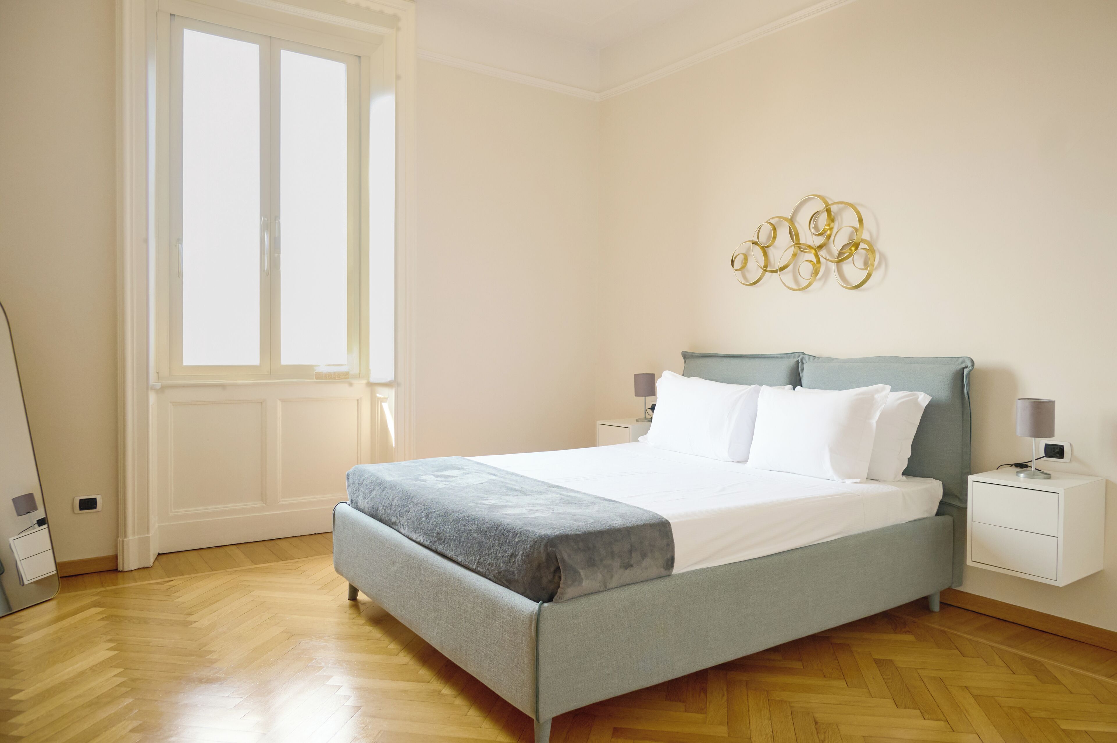 A hotel room with a bed, bedside tables, a lamp, and a wall decoration.