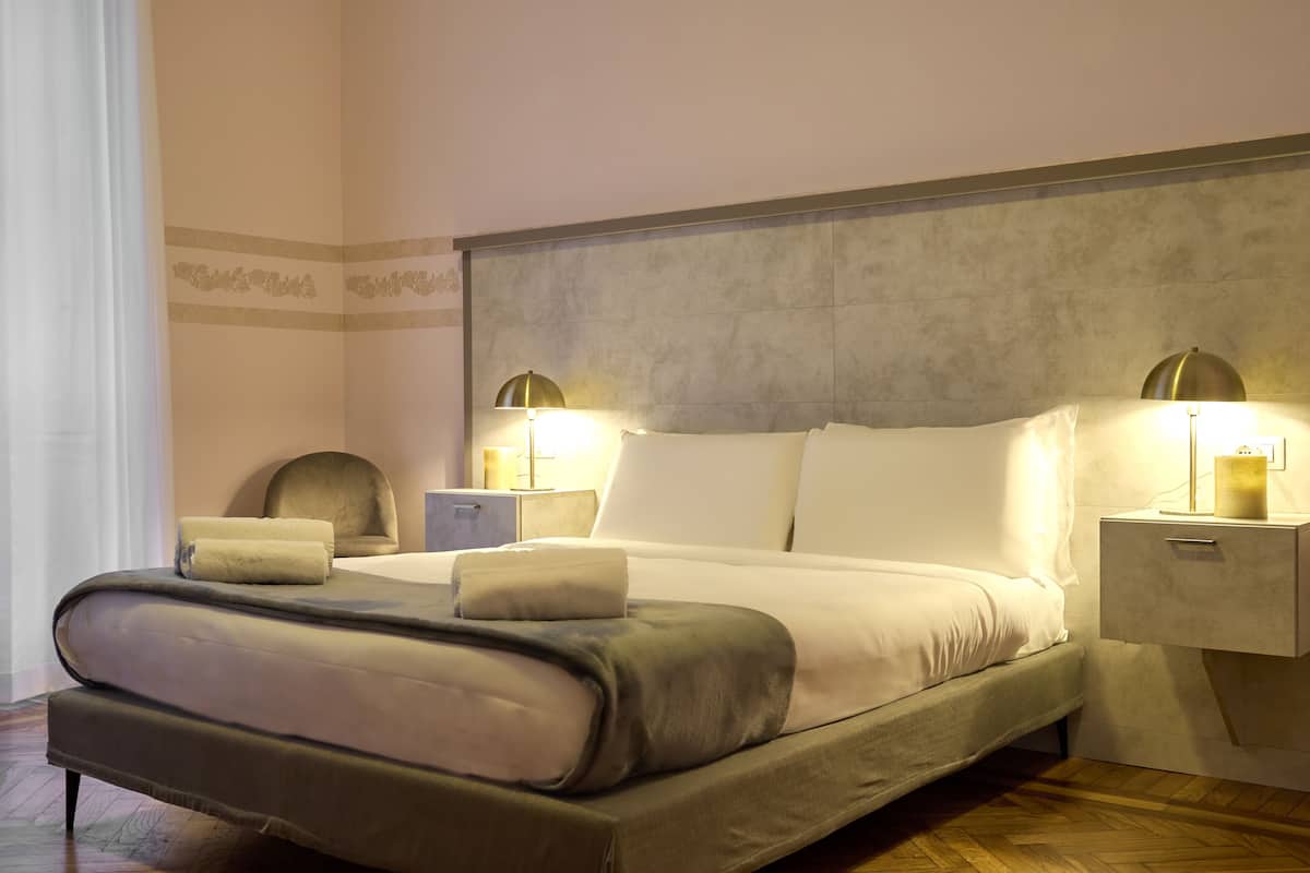 Een keurig opgemaakt bed met een hoofdeinde, twee nachtkastjes met lampen en een klein nachtkastje.