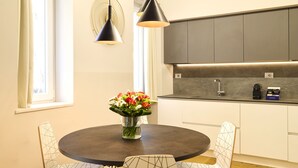A modern kitchen with dark countertops, white cabinets, and a round dining table with two chairs. - Milan Retreats Porta Romana (Milan)