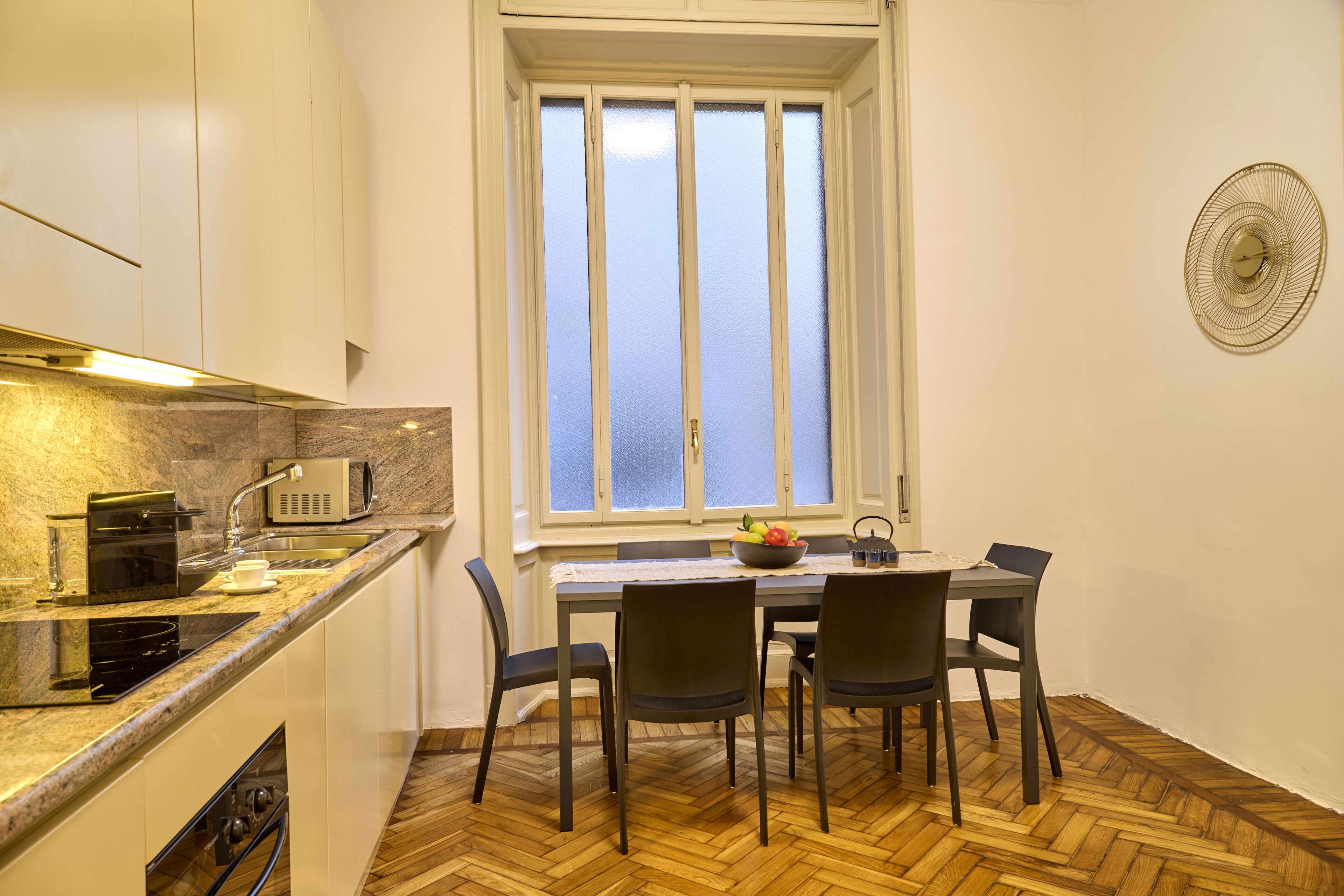 A compact kitchen with a dining area, a window with frosted glass, and a herringbone wood floor.