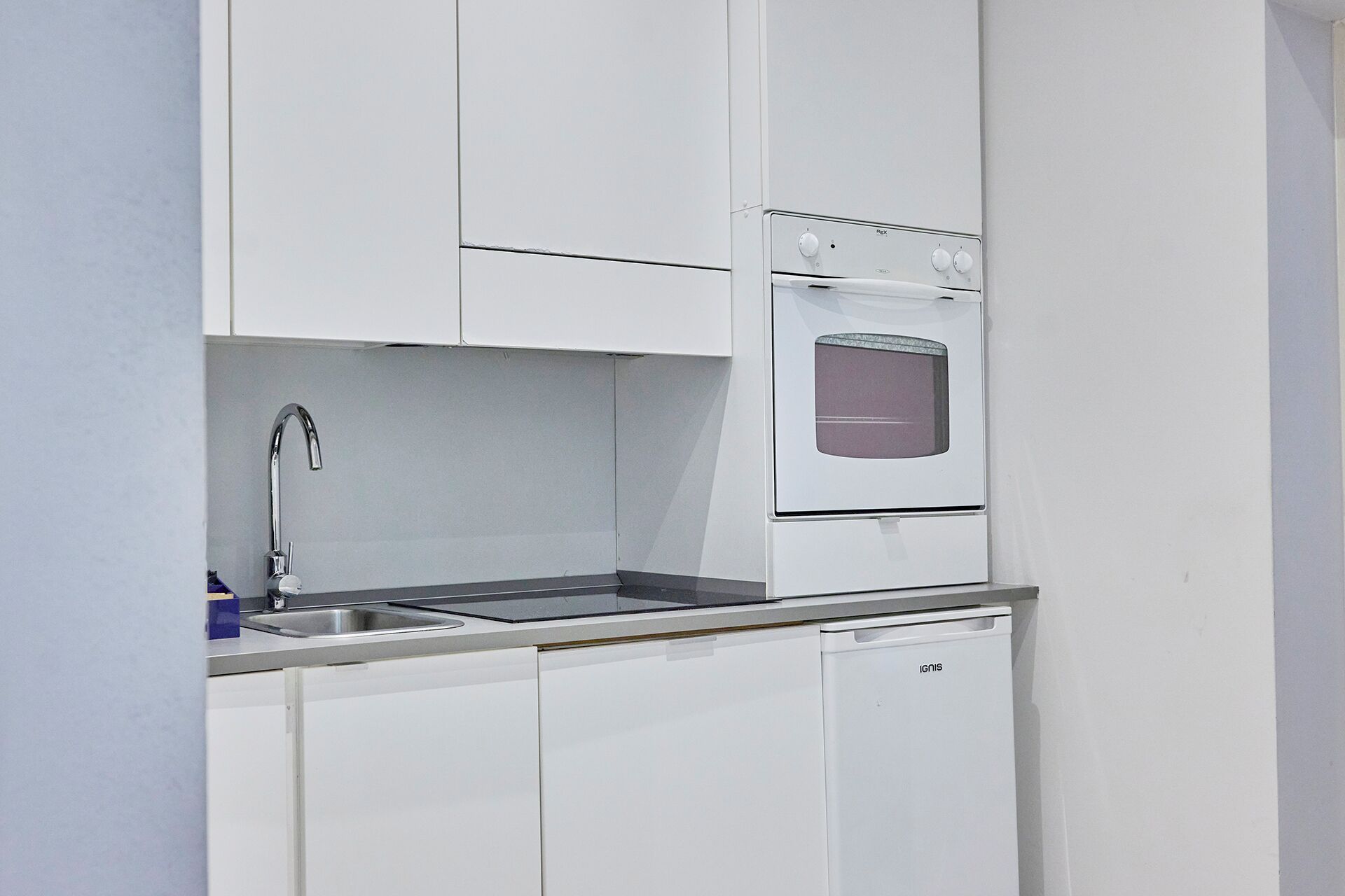 Una cucina compatta con mobili bianchi, un lavello in acciaio inossidabile e un forno integrato.