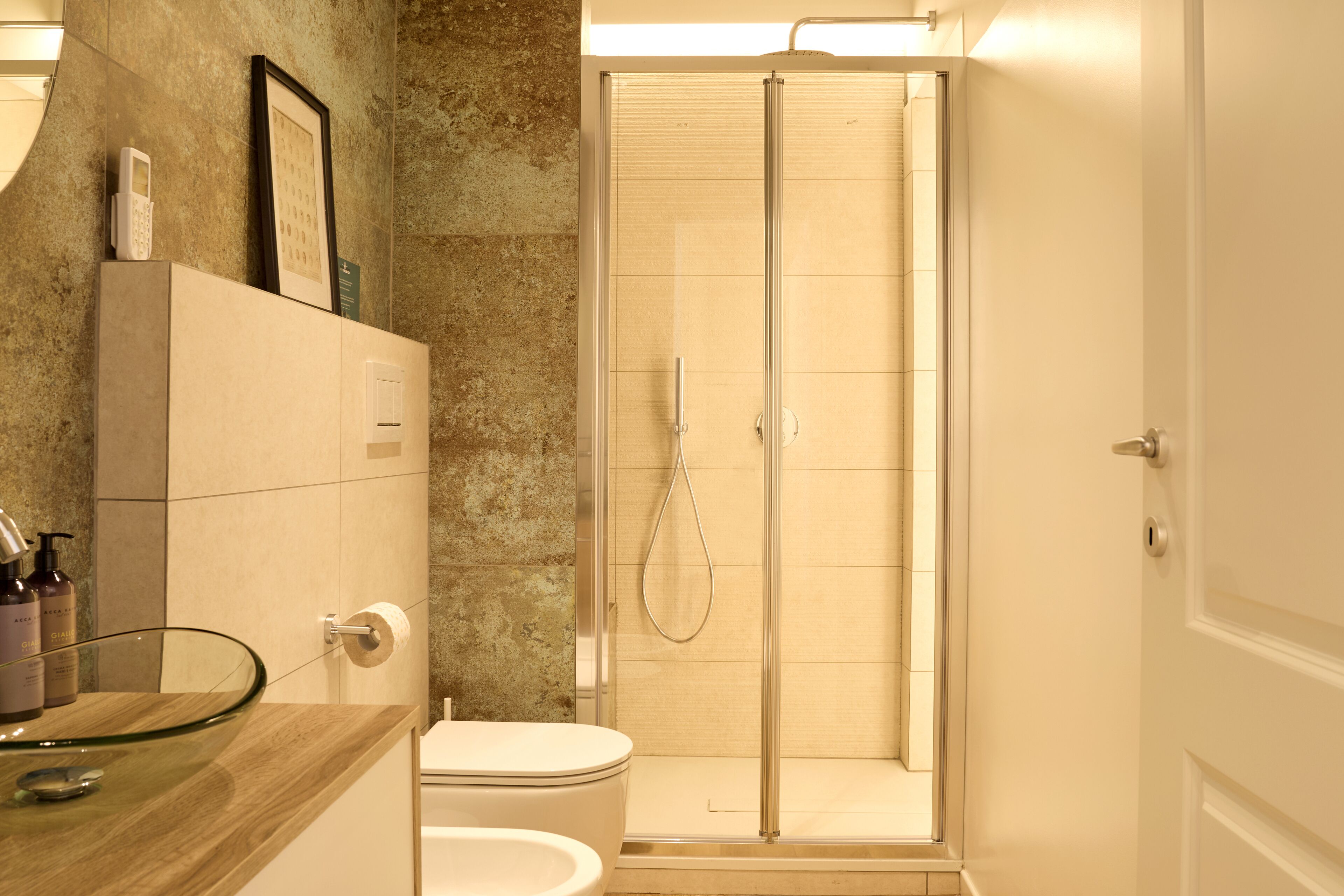 A bathroom with a glass shower enclosure, a toilet, and a vanity with a glass bowl sink.