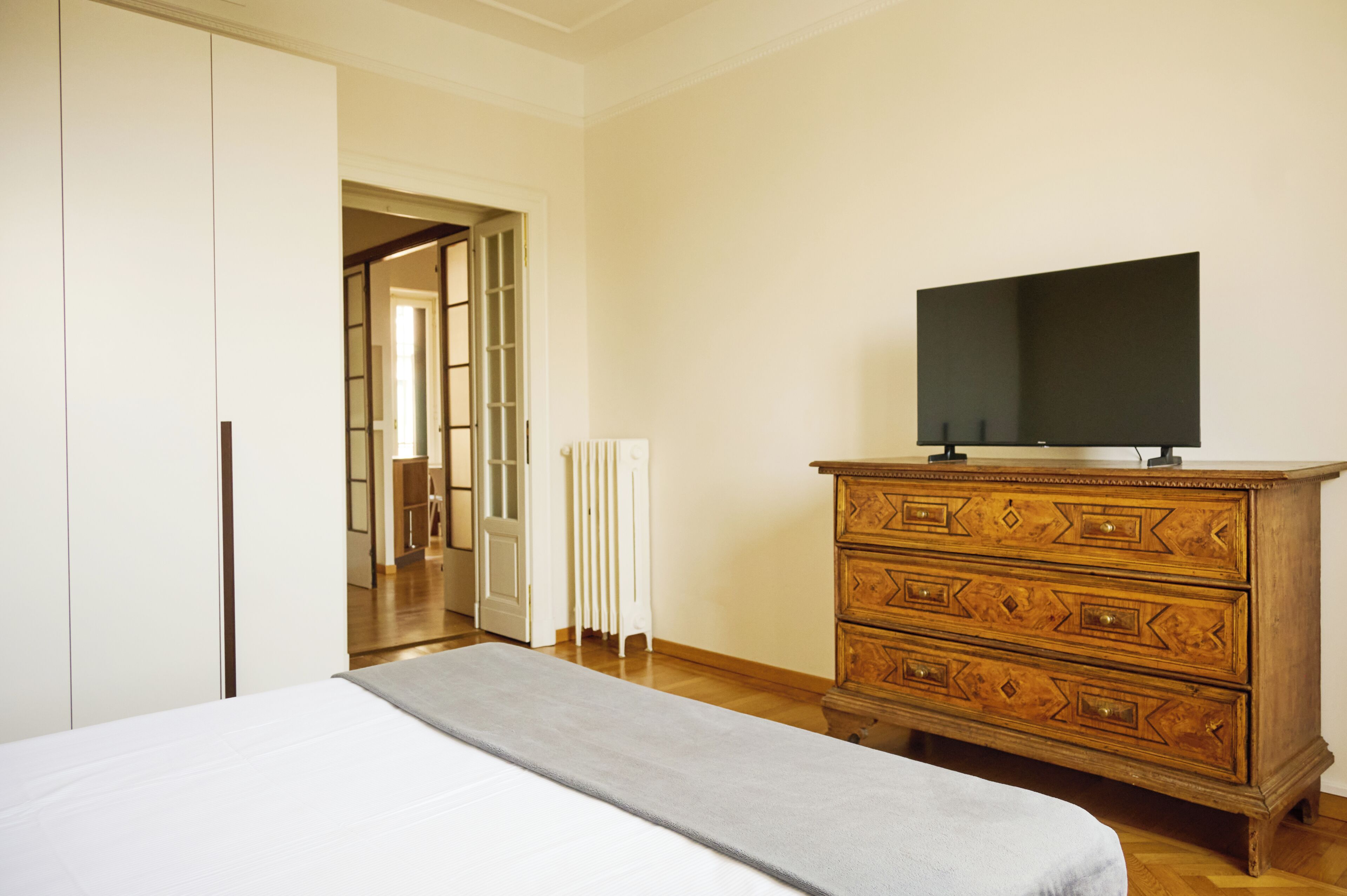 A bedroom with a bed, a dresser, a radiator, and a television.