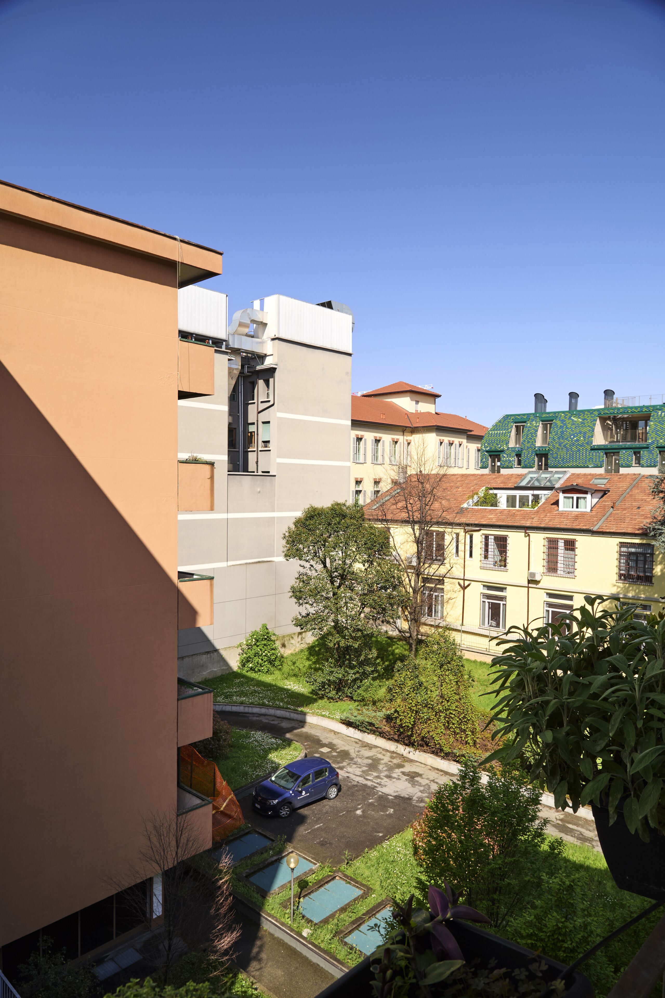 A residential area with a modern building, a parked car, and a small garden.