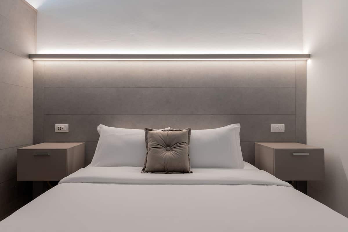 Een moderne slaapkamer met een groot bed, twee nachtkastjes en een wandlamp.