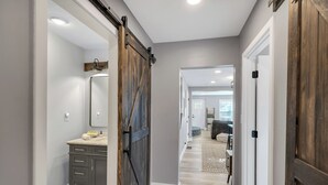 Un pasillo con una puerta de madera estilo granero, un baño con tocador y espejo, y una sala de estar con sofá y alfombra.