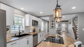 Una cocina moderna con armarios blancos, encimera de madera, estufa de acero inoxidable y una lámpara colgante.