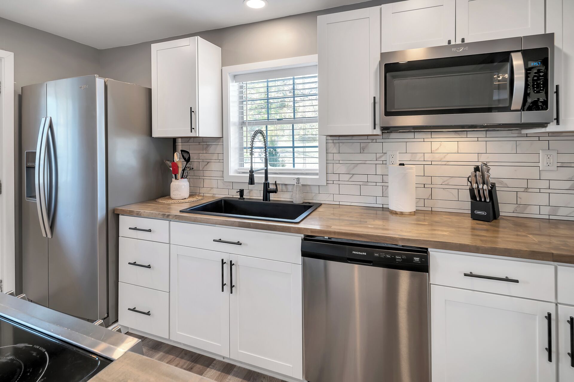 A modern kitchen with stainless steel appliances, white cabinetry, and a window providing natural light.