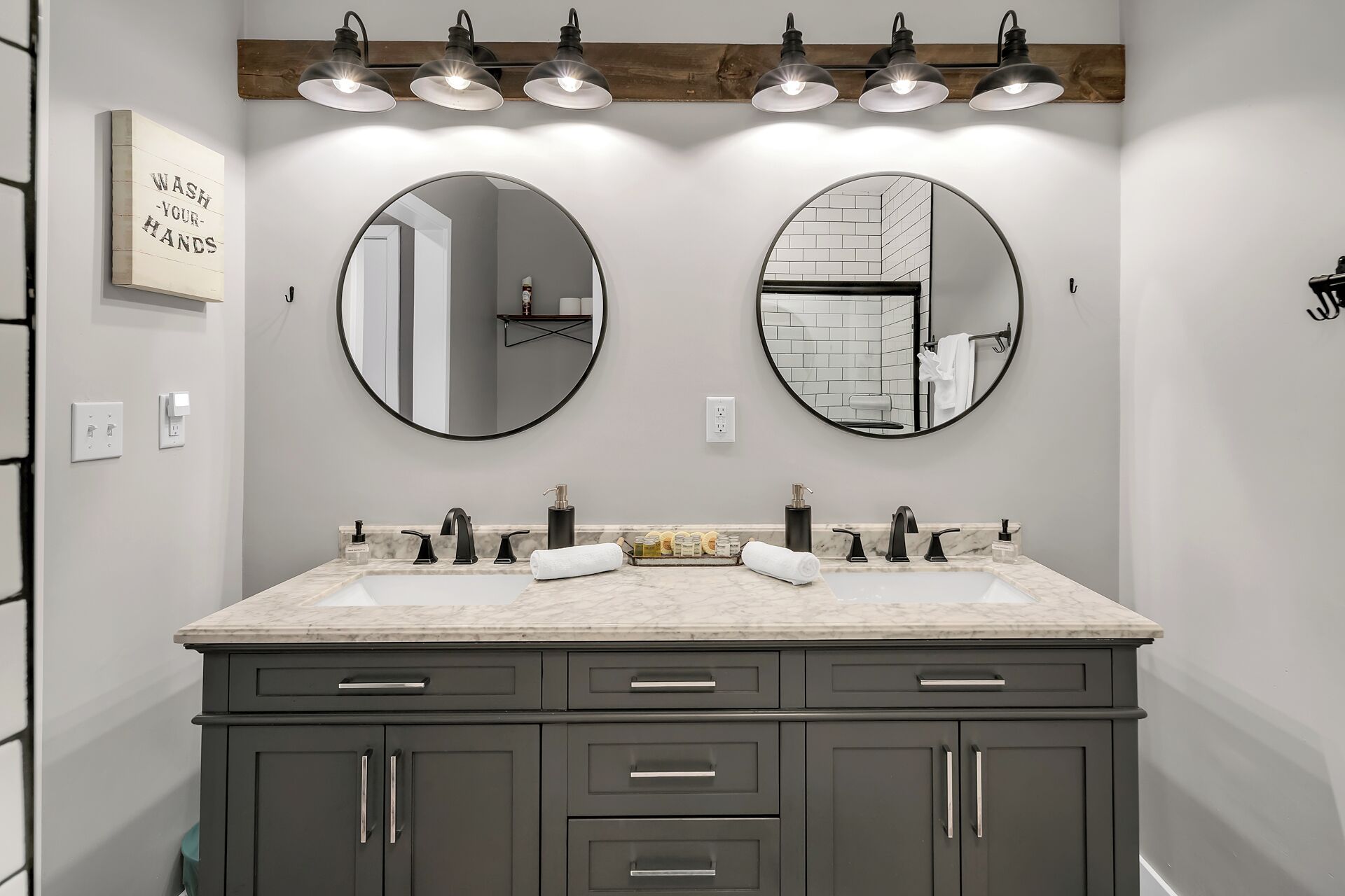 A modern bathroom with two round mirrors, a double sink vanity, and a wooden shelf above the mirrors.