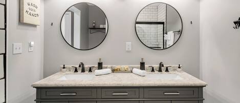 A modern bathroom with two round mirrors, a double sink vanity, and a wooden shelf above the mirrors.