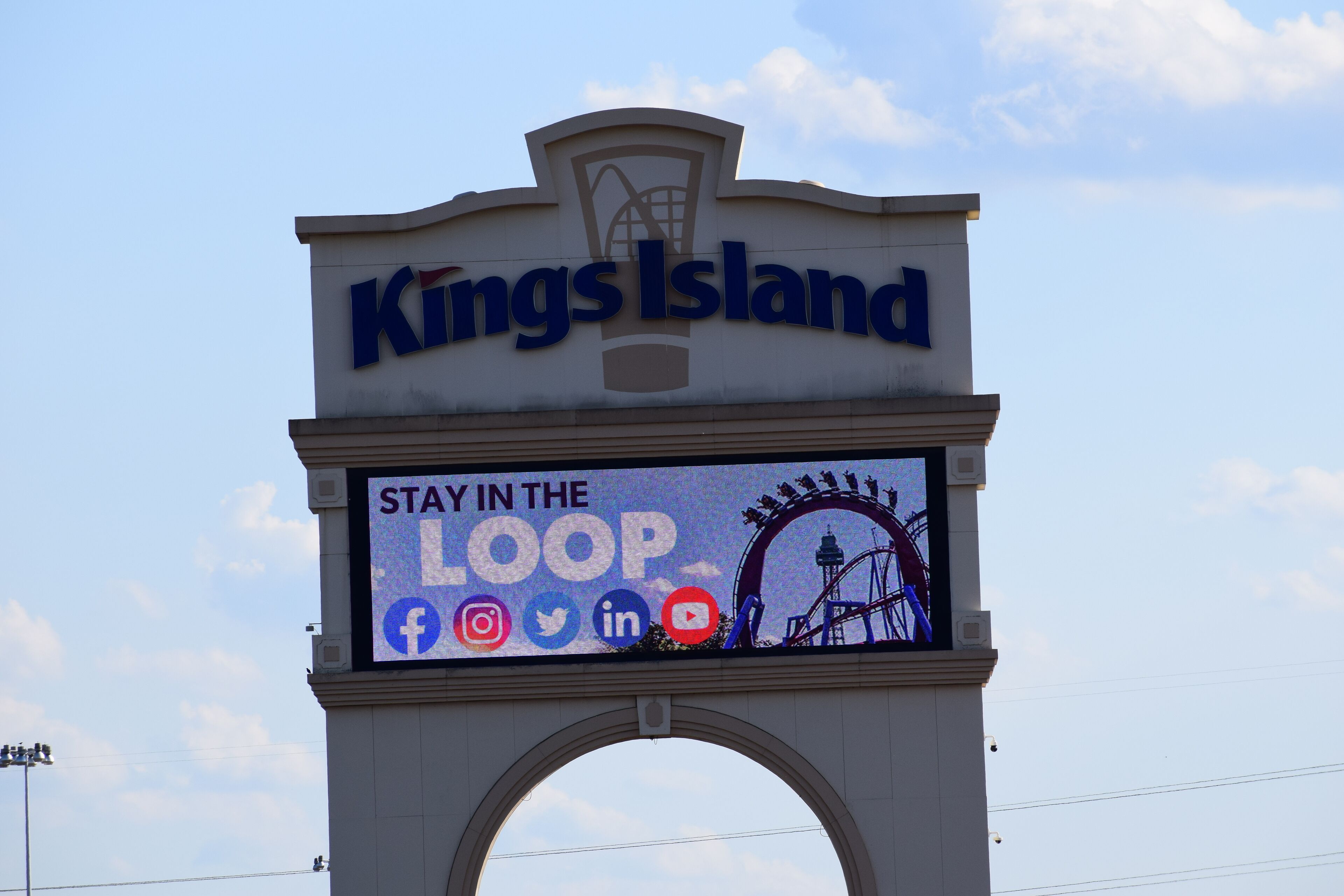 A sign with "Kings Island" and a "Stay in the Loop" advertisement featuring social media icons and a Ferris wheel.