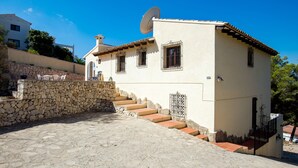 A two-story building with a stone staircase leading to the entrance, a satellite dish on the roof, and a stone wall on the left. - Villa Cezanne, Sea Views, private pool, breezes, WIFI, close to new ALDI (Moraira-Teulada)