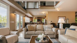 A spacious living room with a large sectional sofa, a coffee table with decorative items, and a view of the kitchen and outdoor area.