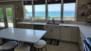A kitchen with a large island, bar stools, a view of the ocean, and a balcony.