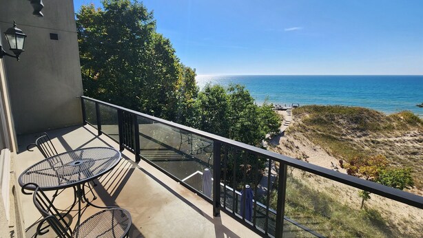A balcony with a table and chairs, overlooking a beach with a clear view of the ocean.