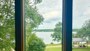 A view through a window of a grassy area with a body of water, trees, and a gazebo. - Portage Lakeside Cabins (Portage Lake)