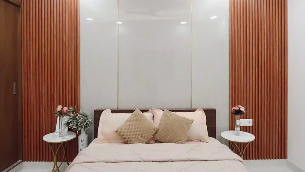 Un dormitorio con una cama, dos mesitas de noche, un florero con flores y persianas verticales.