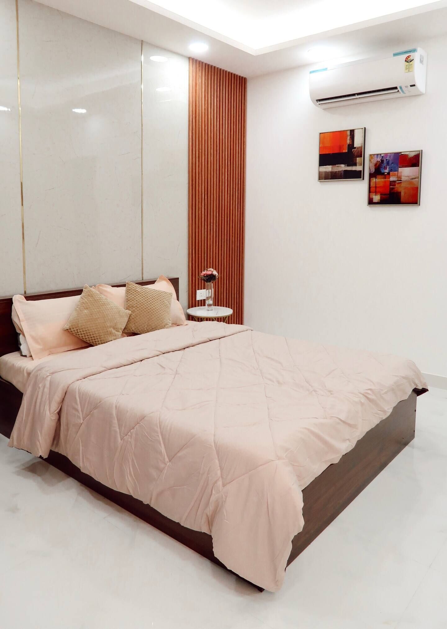 A modern bedroom with a bed, a nightstand, a wall-mounted air conditioner, and two framed artworks.