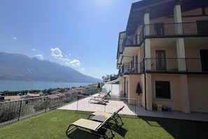 Un balcón con vistas a un lago y montañas, muebles de exterior y un edificio con balcones.