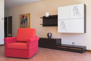 Un salon moderne avec un fauteuil rouge, un meuble noir et une étagère murale ornée d’œuvres d’art.