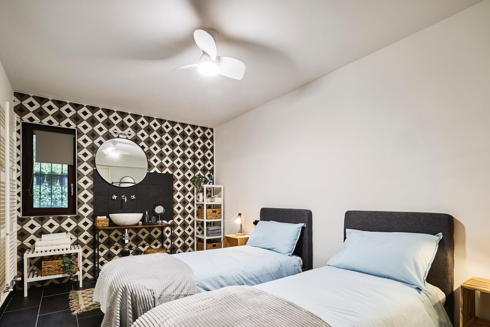 Une chambre avec deux lits, une salle de bain avec un lavabo et un miroir, et des murs décorés de motifs.