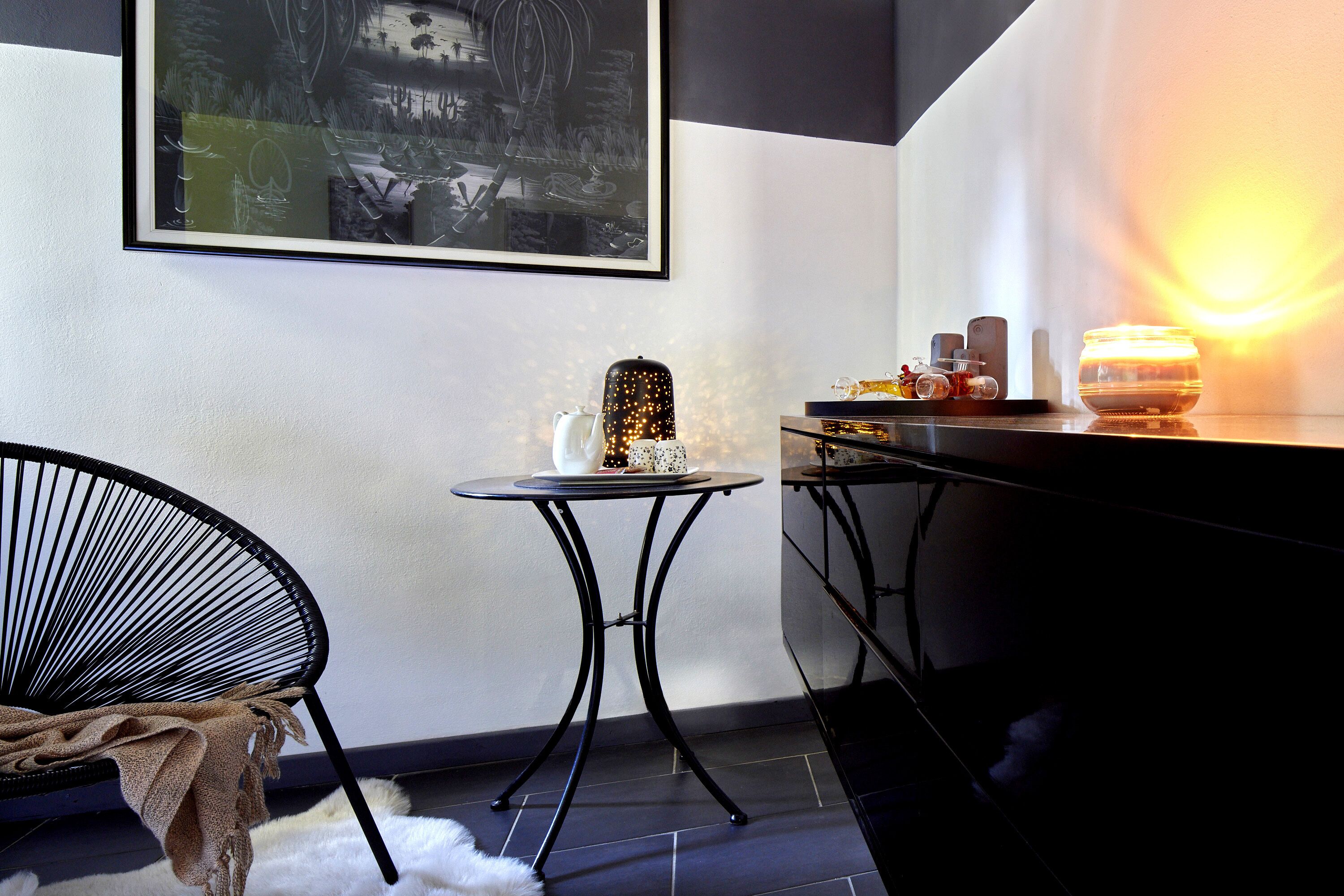 Une pièce moderne avec une chaise noire, une petite table ornée d’un objet décoratif et une œuvre d’art accrochée au mur.